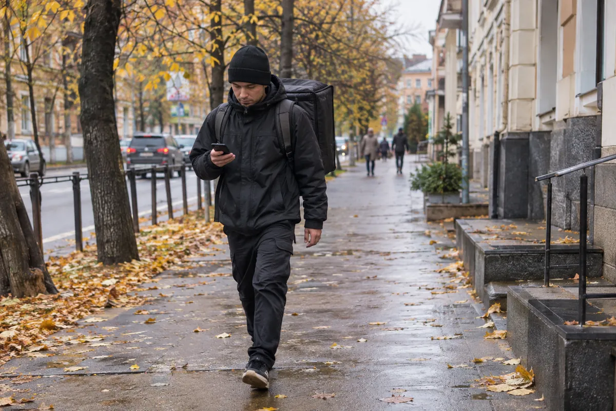 Пеший курьер с термосумкой идёт по улице