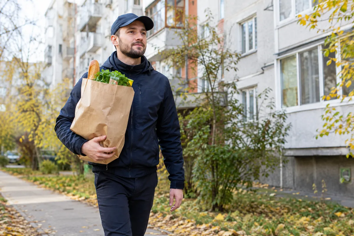 курьер-партнёр несёт пакет с продуктами по жилому кварталу